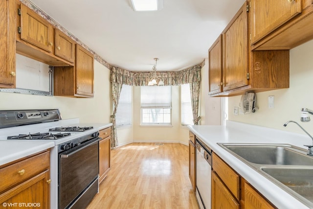 kitchen with white dishwasher, brown cabinets, a sink, light wood-style floors, and gas range oven