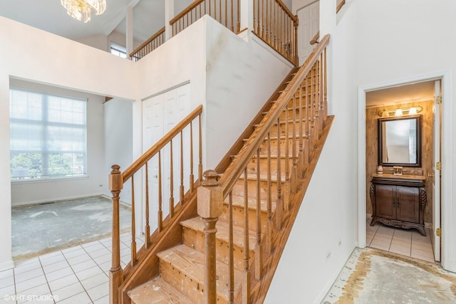 stairs with a high ceiling, tile patterned flooring, carpet floors, a chandelier, and baseboards