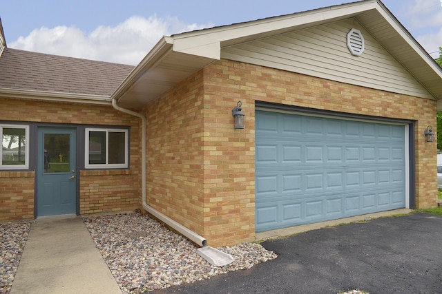 exterior space with roof with shingles, an attached garage, driveway, and brick siding
