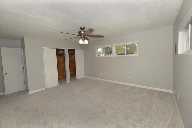 unfurnished bedroom featuring two closets, baseboards, and light colored carpet