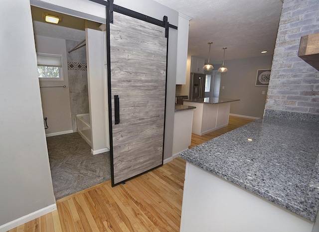 kitchen featuring baseboards, a barn door, white cabinets, light wood finished floors, and decorative light fixtures