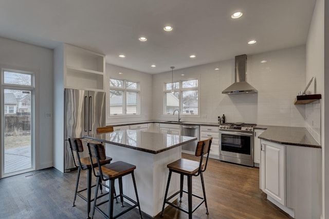 kitchen featuring wall chimney range hood, open shelves, appliances with stainless steel finishes, a sink, and white cabinetry
