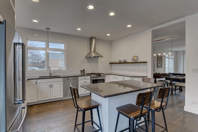 kitchen featuring wall chimney range hood, white cabinets, appliances with stainless steel finishes, a sink, and dark wood-style floors