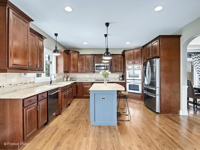 kitchen with stainless steel appliances, arched walkways, a sink, and light wood finished floors
