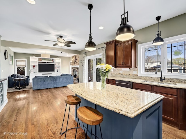 kitchen with light stone countertops, a sink, light wood-style floors, a center island, and a ceiling fan