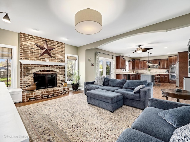 living area with a brick fireplace, wood finished floors, baseboards, arched walkways, and a ceiling fan