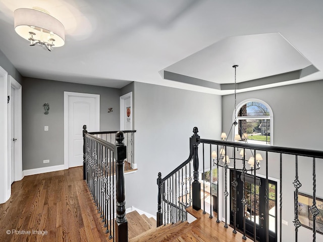 hall featuring baseboards, a notable chandelier, wood finished floors, and an upstairs landing