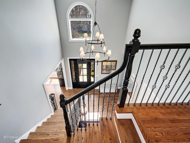 stairs with an inviting chandelier, baseboards, a high ceiling, and wood finished floors