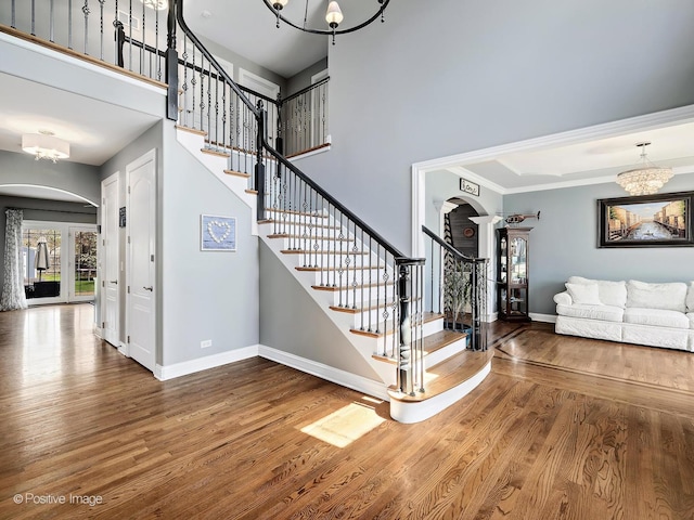 stairs featuring arched walkways, baseboards, an inviting chandelier, and wood finished floors