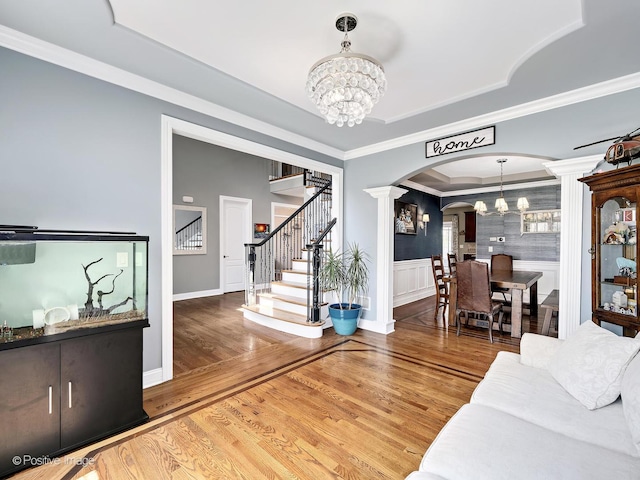 living area featuring crown molding, arched walkways, stairway, and a notable chandelier