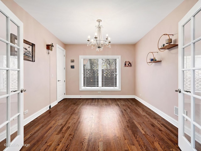 unfurnished dining area featuring baseboards, a notable chandelier, and dark wood-style floors