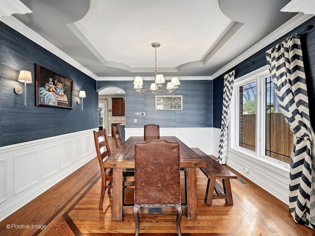dining room featuring a healthy amount of sunlight, arched walkways, wainscoting, and a tray ceiling