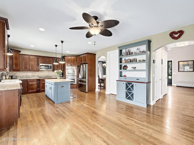 kitchen with ceiling fan, light wood-style floors, arched walkways, stainless steel appliances, and a kitchen island
