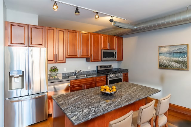 kitchen with a sink, dark stone counters, stainless steel appliances, a kitchen bar, and a kitchen island