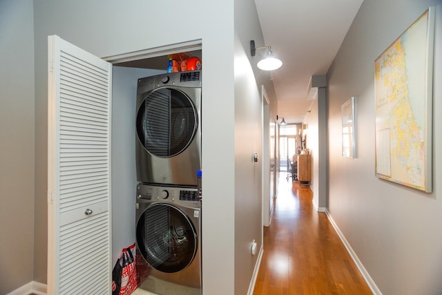 laundry room featuring laundry area, baseboards, wood finished floors, and stacked washer / dryer