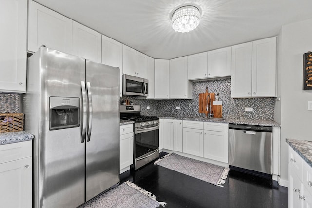 kitchen with light stone countertops, a chandelier, white cabinets, tasteful backsplash, and stainless steel appliances