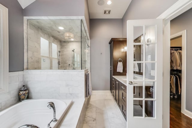 bathroom featuring a shower stall, a bath, a walk in closet, vanity, and baseboards