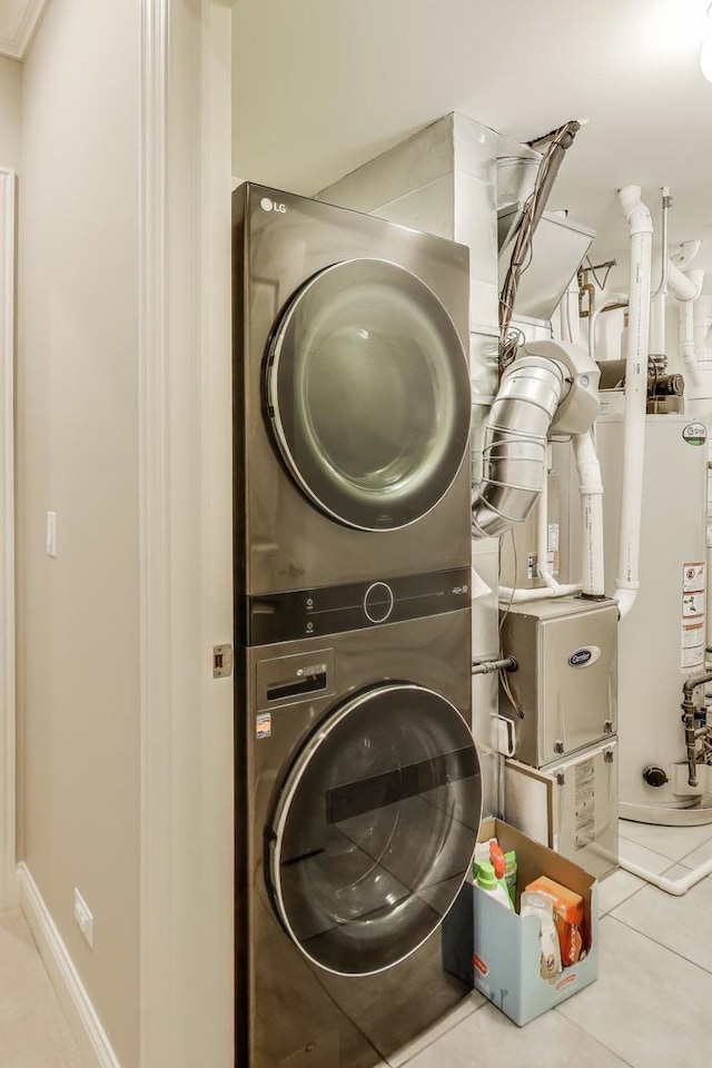 clothes washing area featuring stacked washing machine and dryer, tile patterned flooring, and water heater