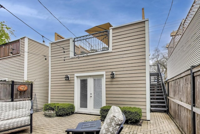 rear view of property with fence, a patio, stairs, french doors, and a balcony