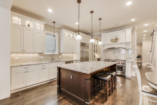 kitchen featuring premium appliances, a sink, decorative backsplash, a center island, and white cabinets