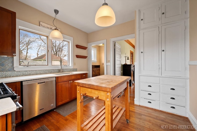 kitchen with stainless steel dishwasher, pendant lighting, light countertops, a sink, and light wood finished floors