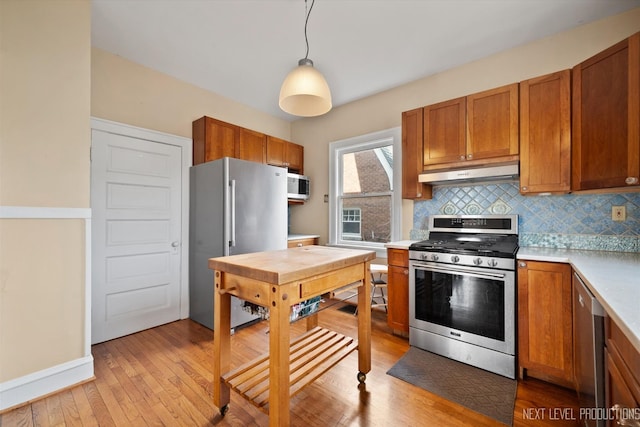 kitchen featuring under cabinet range hood, brown cabinets, appliances with stainless steel finishes, and light countertops