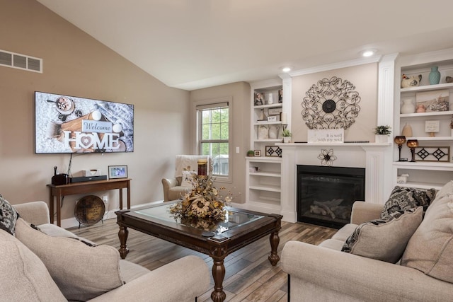 living area with wood finished floors, a glass covered fireplace, lofted ceiling, and built in features