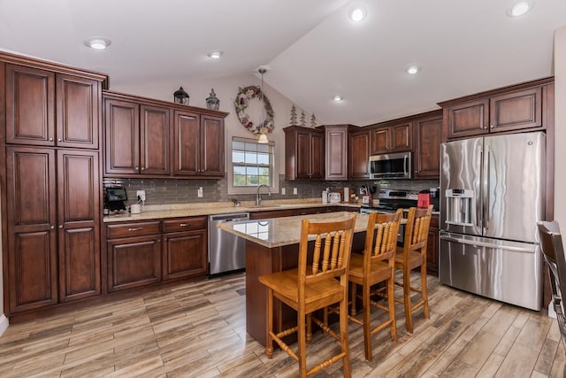 kitchen featuring appliances with stainless steel finishes, lofted ceiling, a sink, light wood-style floors, and a kitchen island