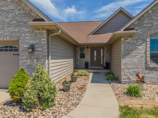 entrance to property with a garage, a shingled roof, and brick siding