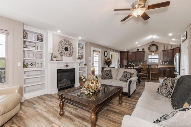 living area with light wood-style flooring, a ceiling fan, a glass covered fireplace, vaulted ceiling, and recessed lighting