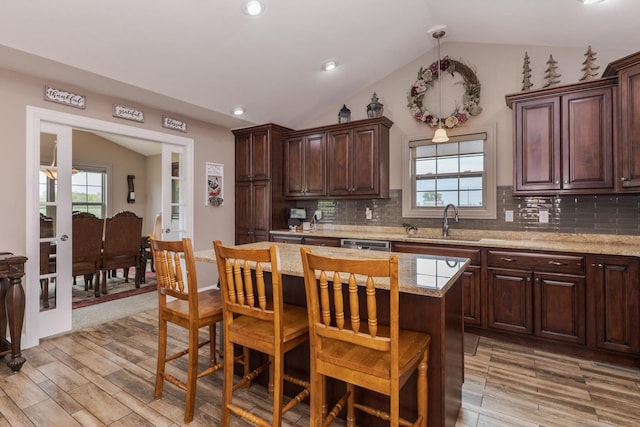 kitchen with a sink, light wood-style floors, vaulted ceiling, a kitchen breakfast bar, and backsplash