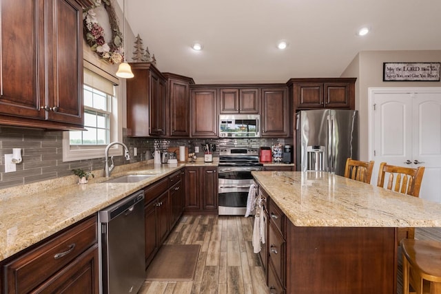 kitchen featuring stainless steel appliances, a sink, a breakfast bar, a kitchen island, and light stone countertops