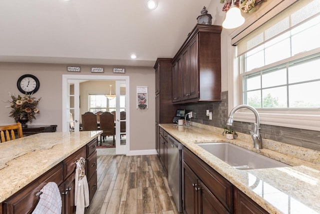 kitchen with a sink, stainless steel dishwasher, decorative backsplash, light wood-style floors, and baseboards