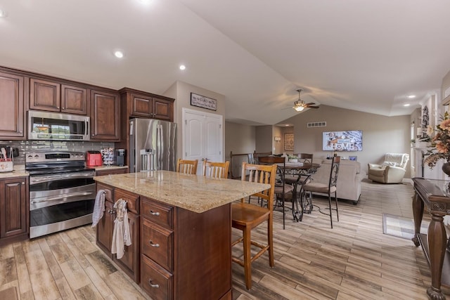 kitchen with stainless steel appliances, a kitchen bar, lofted ceiling, ceiling fan, and open floor plan