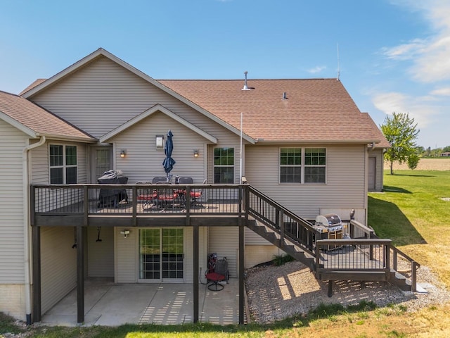 rear view of property with a patio, a wooden deck, a lawn, roof with shingles, and stairs