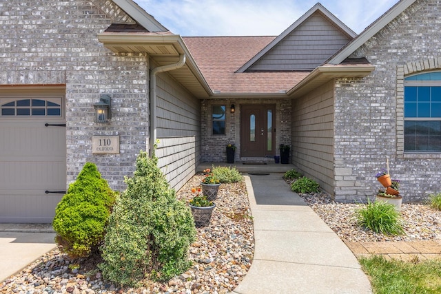 view of exterior entry with roof with shingles, brick siding, and an attached garage