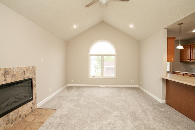 unfurnished living room with a ceiling fan, light colored carpet, a tiled fireplace, vaulted ceiling, and baseboards