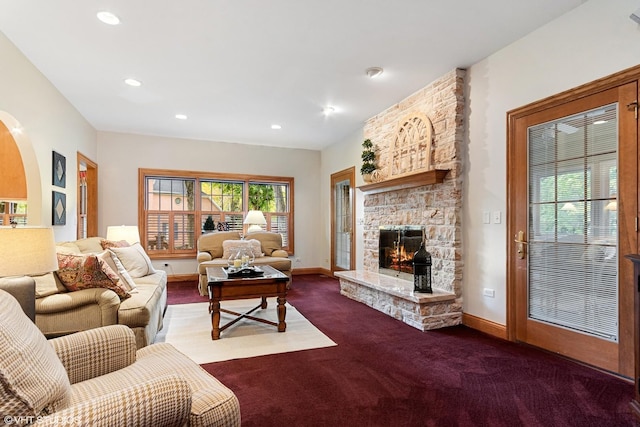 carpeted living area featuring arched walkways, a stone fireplace, baseboards, and recessed lighting
