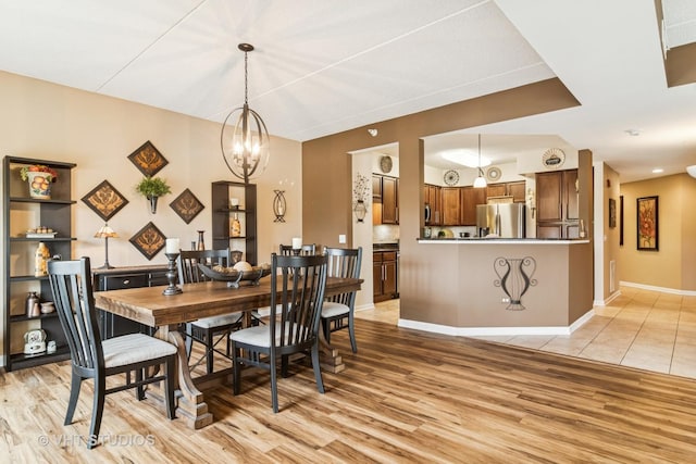 dining area with baseboards, an inviting chandelier, and light wood-style flooring
