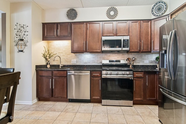 kitchen featuring appliances with stainless steel finishes, a sink, dark stone counters, light tile patterned floors, and backsplash