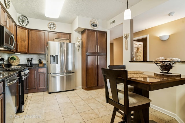 kitchen featuring visible vents, hanging light fixtures, tasteful backsplash, light tile patterned floors, and stainless steel appliances