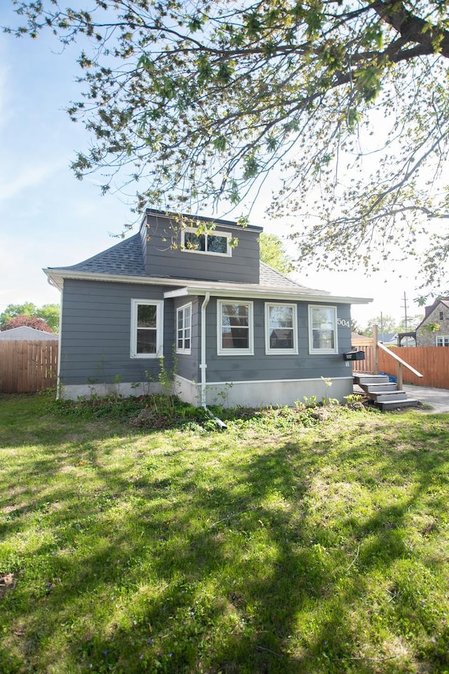 view of front of house featuring a shingled roof, a front lawn, and fence