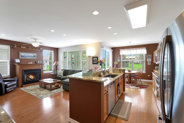 12951 Bull Ridge Dr, Huntley, IL 60142 - kitchen featuring a kitchen island with sink, a lit fireplace, a sink, light wood-style floors, and stainless steel appliances