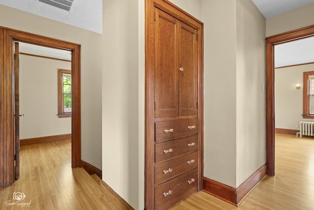 corridor featuring radiator heating unit, baseboards, and light wood-type flooring