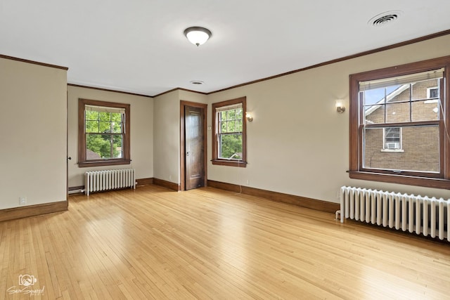 spare room with radiator heating unit, ornamental molding, baseboards, and light wood-style floors
