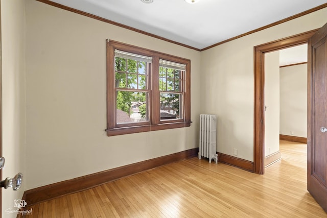spare room featuring radiator, light wood-style flooring, baseboards, and crown molding