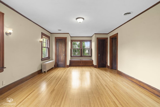 empty room featuring radiator heating unit, ornamental molding, light wood finished floors, and baseboards