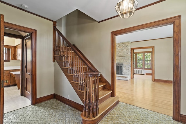 stairs with radiator heating unit, a fireplace, a chandelier, baseboards, and crown molding
