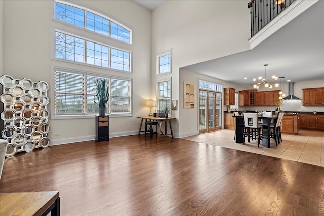 living area with an inviting chandelier, light wood-style floors, a towering ceiling, and baseboards