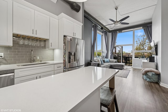 kitchen with stainless steel fridge, a ceiling fan, a sink, backsplash, and light countertops